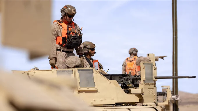 Marines ride in a light armored tactical vehicle equipped with a crew-served weapon during motorized operations training in a desert environment.