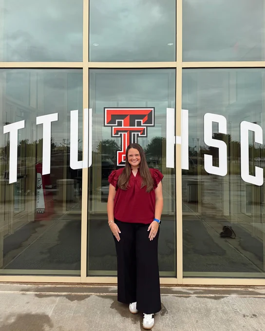 Female physical therapy student stands outside in front of a window decorated with the TTUHSC logo.