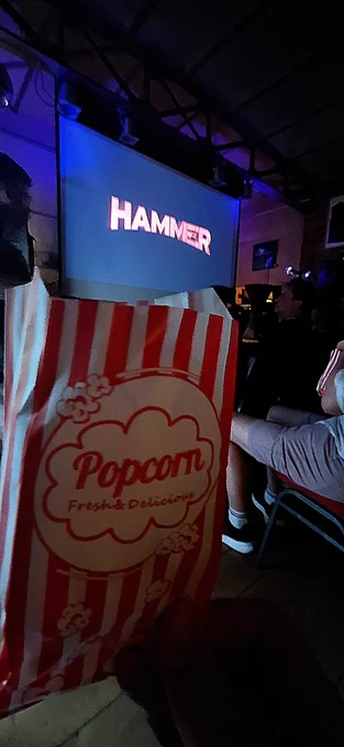 Auf der Leinwand im Hintergrund steht der Name "Hammer", im Vordergrund ist eine Tüte mit Popcorn zu sehen. 