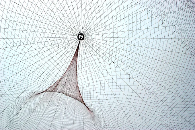 Detalhe da instalação “She Changes”, de Janet Echelman, vista de baixo, com a rede têxtil suspensa iluminada pela luz natural.