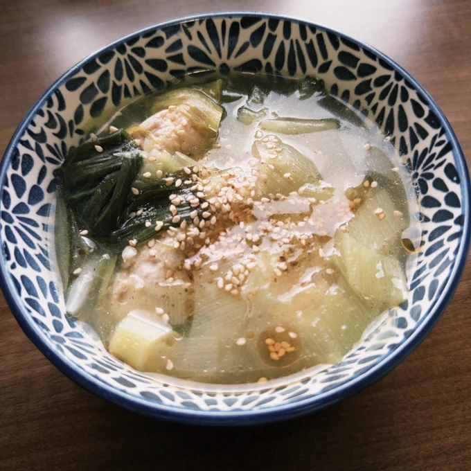 ネギと手羽先が入った透明なスープの写真。 白胡麻とごま油が浮いていて、とろっとして見える。白地に紺色で花の模様が描かれているスープボウルに入っている。