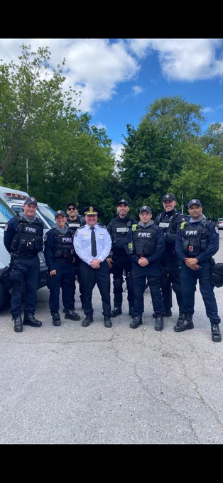 The Toronto Fire Chief standing alongside Toronto Fire Services Public Order Unit members. They are dressed in POU gear and the Fire Chief in white shirt, blue pants and and cap.