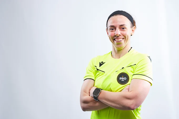 An individual wearing a bright yellow sports uniform with black accents, standing confidently with arms crossed. The uniform has a "PRO" logo on the chest. The background is a plain light color.