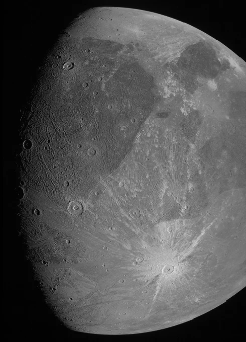 High-resolution black and white photo of a moon, focusing on its heavily cratered surface with various sizes and depths of impact marks, showcasing detailed geological features that highlight the textured terrain.
