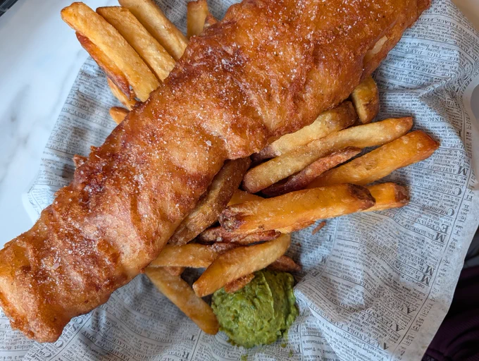 A large fillet of beer battered fried fish sits on top of thick crispy fries with a side of guacamole. Mmmm