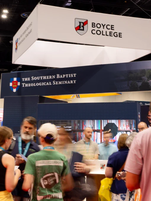 A busy convention scene featuring the Boyce College and Southern Baptist Theological Seminary booths. People are engaging in conversation, suggesting an informative and interactive atmosphere.