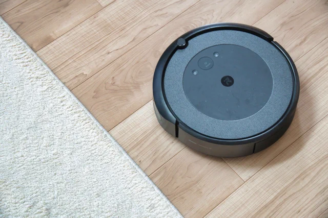 木の床と白いラグの上に置かれた黒いロボット掃除機