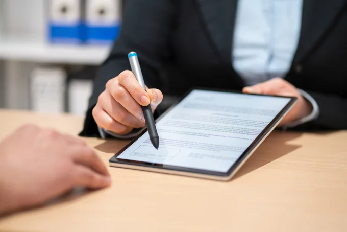 Person using a stylus to review and annotate a document displayed on a tablet during a meeting.