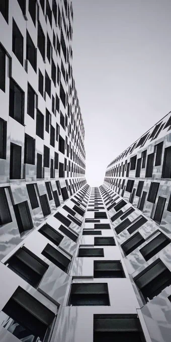 A dramatic low-angle lookup view of the distorted, white grid facade and staggered black windows of the Upper West tower in Berlin, looking up toward a grey sky.