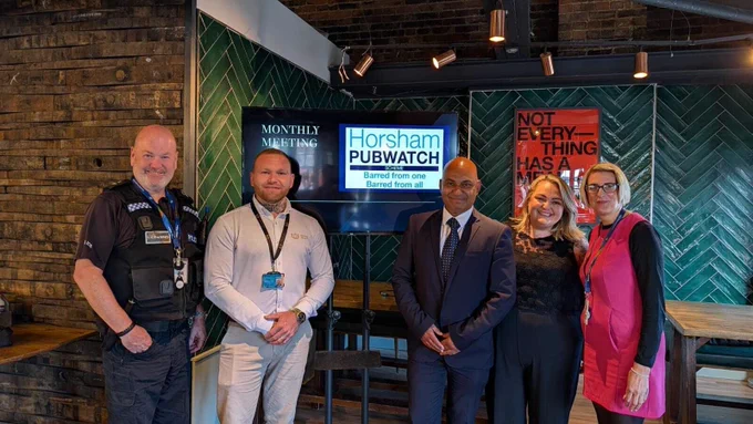 Five people standing in a row facing the camera in front of a presentation on a tv screen. Pictured (from L to R): PC Marvin Lucas (West Sussex Licensing team), Chris Maldon chair of the Horsham Pubwatch, Abs Haque, Jodie Munday licensee of Horsham Brewery & Tap Room and Lisa Hunt (West Sussex Licensing team). 