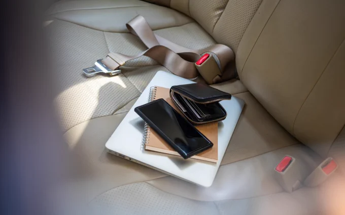 A laptop, phone, wallet, and seatbelt are on a car seat.