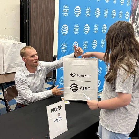 An AT&T volunteer hands a donated laptop to a student