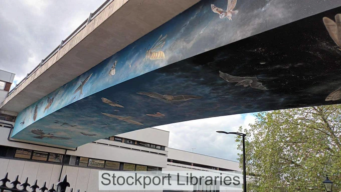 Mural of birds, a bee, and bats flying under a concrete flyover, set against a sky background.