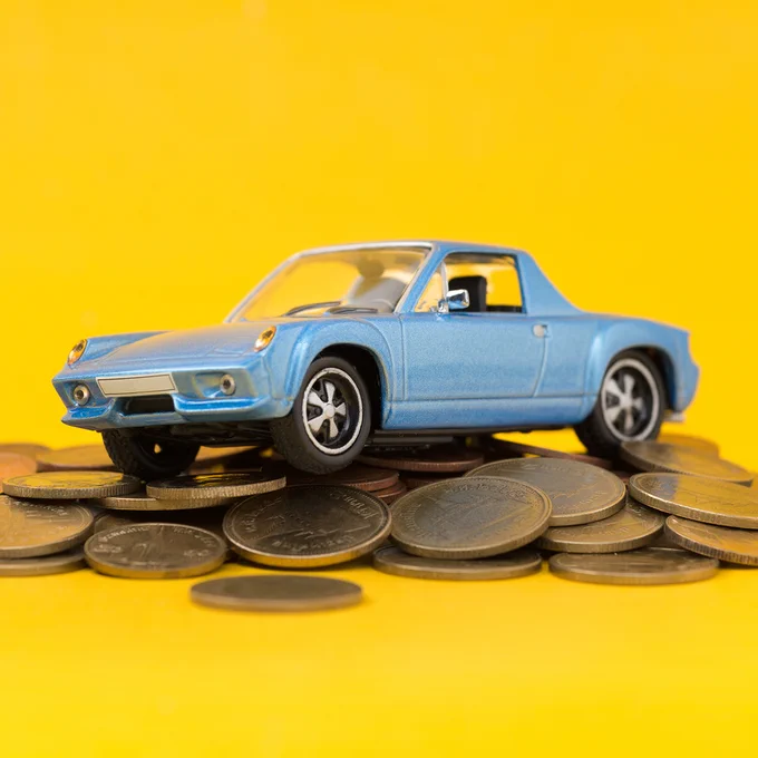 A small blue toy car is placed on top of a pile of coins against a bright yellow background.