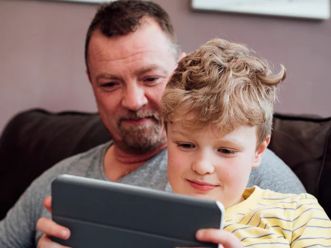 A father and son sat on the sofa and looking at a mobile phone.