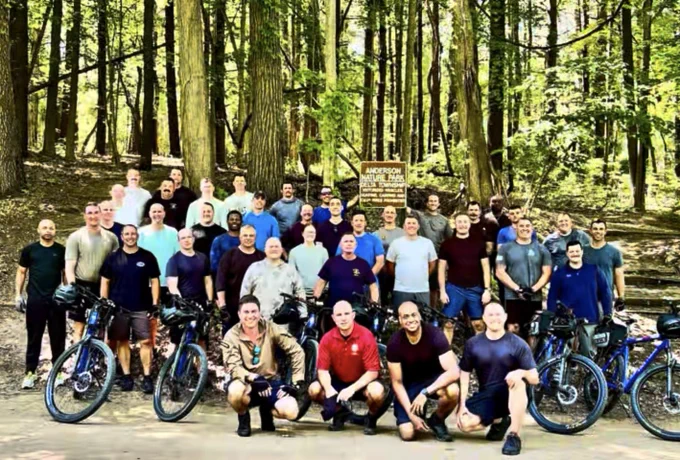 Photograph of the 35 Michigan State Police members with 4 bicycles in front of a wooded area. 