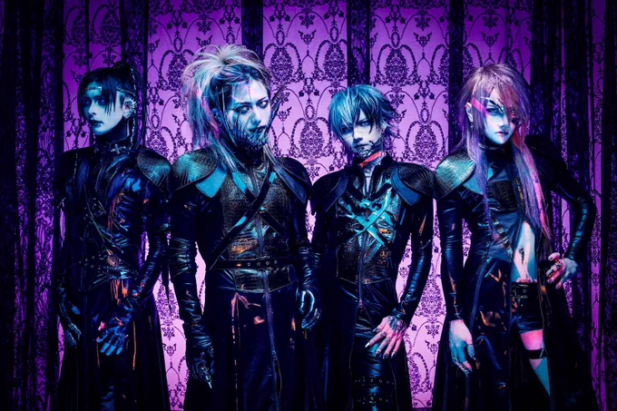 The photo features the four members of JILUKA, dressed in distinct dark, gothic attire with silver face jewellery (such as a chin, eye or ear piece) posing against a purple gothic-themed screen. © DPR Japan/FAIZH Music