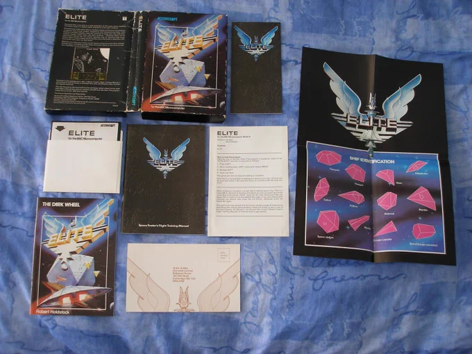 BBC Elite (Acornsoft, 1984) - retail box contents, including the following:-
1. Space Traders Flight Training Manual
2. Dark Wheel novella
3. Ship identification poster
4. Summary of controls and ship identification card
5. Game disc
6. Competition entry card
7. Loading instructions