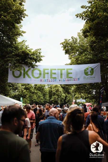 Foto vom Eingangsbereich der Ökofete. Über den Gehweg ist ein großes Banner gespannt. Auf dem Banner steht:"Ökofete; Herzlich Willkommen". Auf dem Weg sind sehr viele Menschen unterwegs.