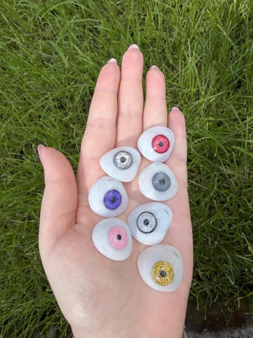 A girl is holding 7 bespoke eyes in her hand. They are colourful and some are also glittery.