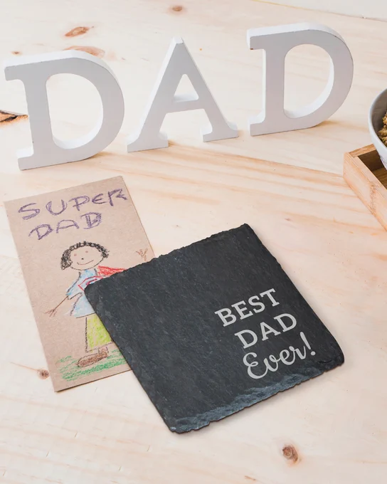 Custom Granite Stone Coaster Engraved With Best Dad Ever Text Displayed On Wood Table With Child Drawing And Dad Letter Decor