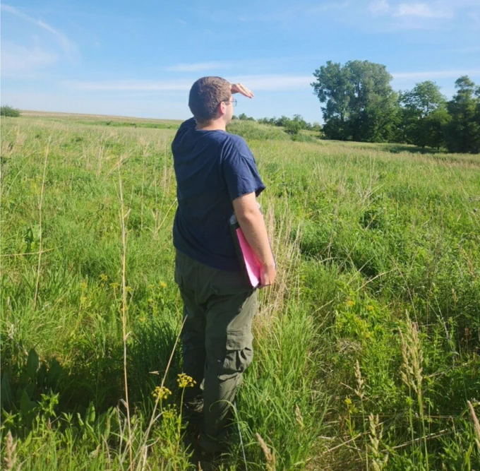 Paxton standing in a field searching for pollinators. 