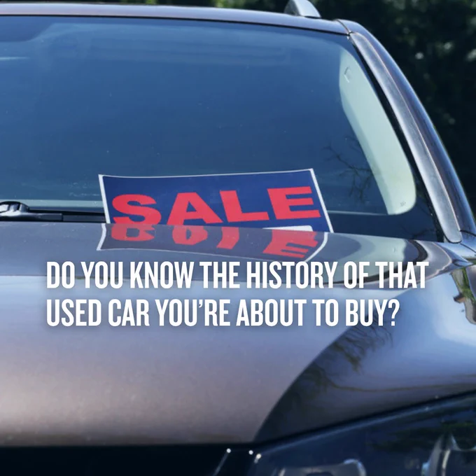 Close-up of a used car windshield with a red SALE sign and a question about knowing the car's history before purchase.