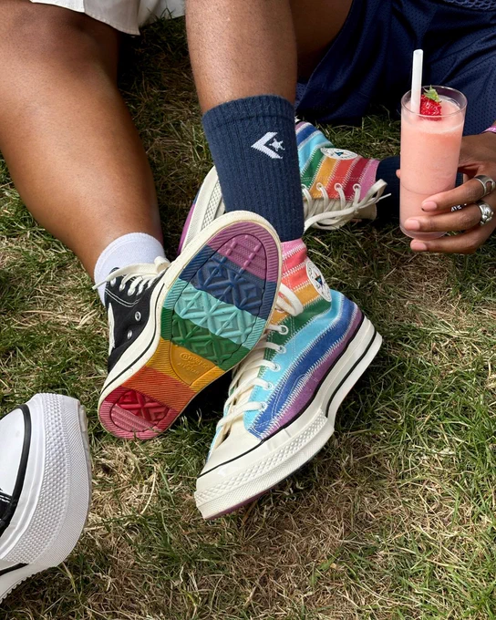 An image of multiple people's lower legs wearing pairs of Converse trainers whilst sitting on grass.