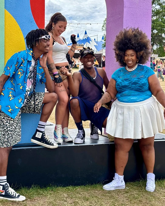 An image of four people wearing pairs of Converse trainers with summery outfits whilst standing on a platform at Mighty Hoopla festival. 