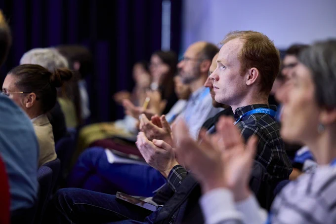 Audience members seated in rows clapping during an indoor event or presentation.