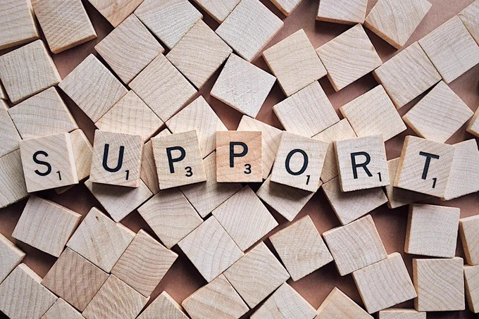 The word SUPPORT spelled out with wooden Scrabble tiles on a background of scattered blank tiles.