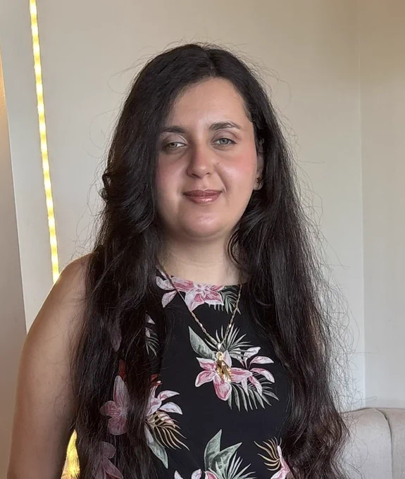 Professional photo of Mariam Fahmy wearing a black, flower-patterned dress and gold necklace.