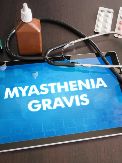 A tablet displaying the text "Myasthenia Gravis" rests on a table. Surrounding it are a stethoscope, medicine bottle, and blister packs of pills.