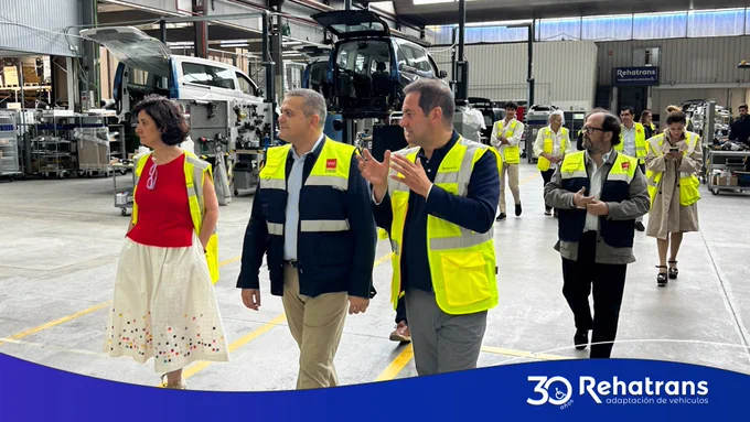 Personas con chalecos reflectantes recorren una fábrica de adaptación de vehículos con furgonetas y equipos.