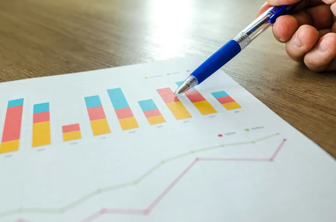 A hand points a blue pen at a colorful bar chart on a printed report.