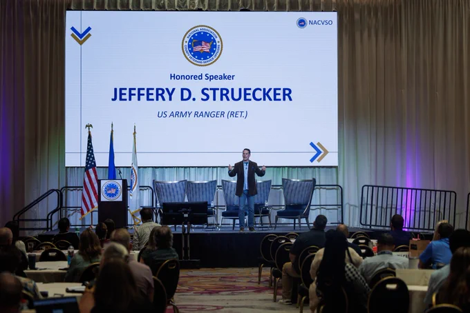 A keynote speech being delivered by a distinguished retired US Army Ranger at a formal event. Attendees seated and listening intently.