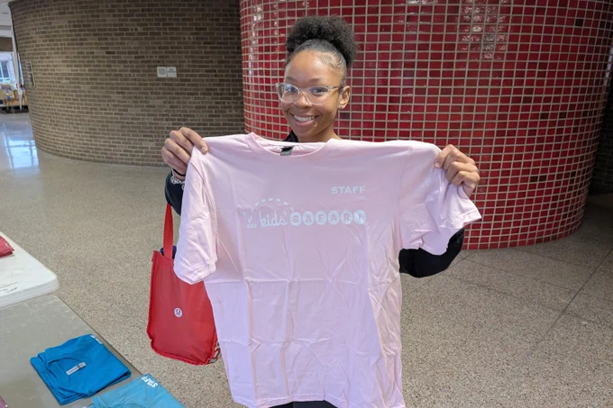 A high school student holding up a Kids' SAFARI staff T-shirt at a training event for the summer program.