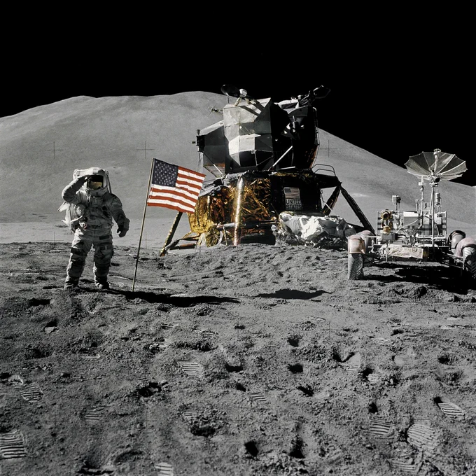 L'astronaute James Irwin se tient près du module lunaire Falcon sur la Lune durant Apollo 15. À droite de l'image se trouve le rover lunaire, utilisé pour la première fois dans une mission Apollo. Le drapeau américain est planté devant le LM, tandis que les montagnes de la région de Hadley-Apennine s'élèvent à l'arrière-plan sous un ciel noir.