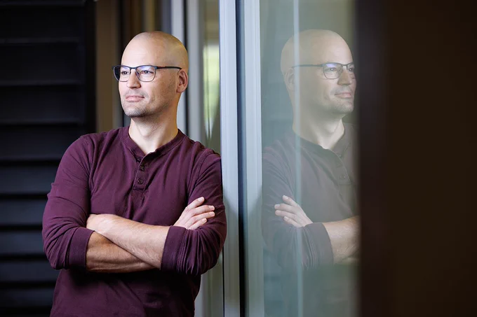 Jonathan Campbell, standing inside near a reflective glass surface, appearing thoughtful.