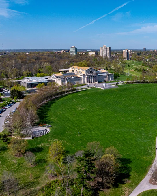 An aerial shows the Saint Louis Art Museum on top of Art Hill separates the Emerson Grand Basin in the foreground from a landscape of spring trees underneath a blue sky behind the building