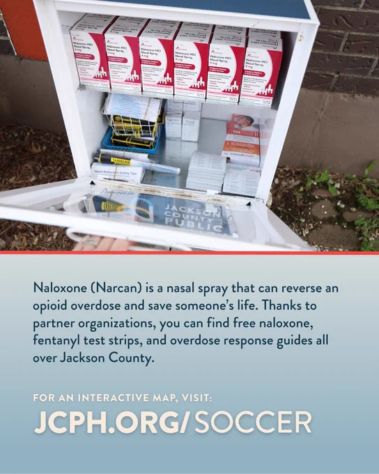 Open outdoor porch box containing boxes of Naloxone nasal spray, fentanyl test strips, and overdose response guides. A sign mentions Jackson County Public Health. Text provides information on obtaining these supplies and directs to JCPH.org/soccer for a map.