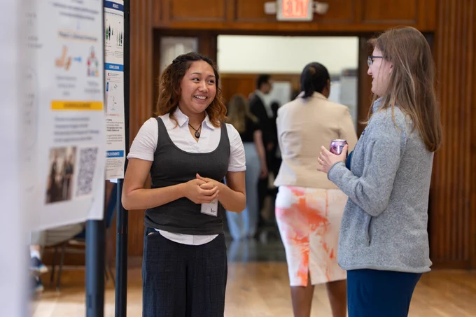 Two women talking in front of research poster.