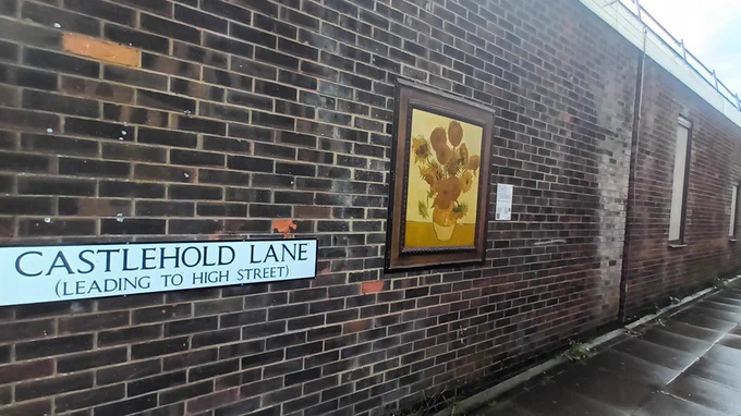 Van Gogh's Sunflowers hanging on a brick wall on Castlehold Lane in Newport, Isle of Wight. Don't worry: it's not the original out in that rain.