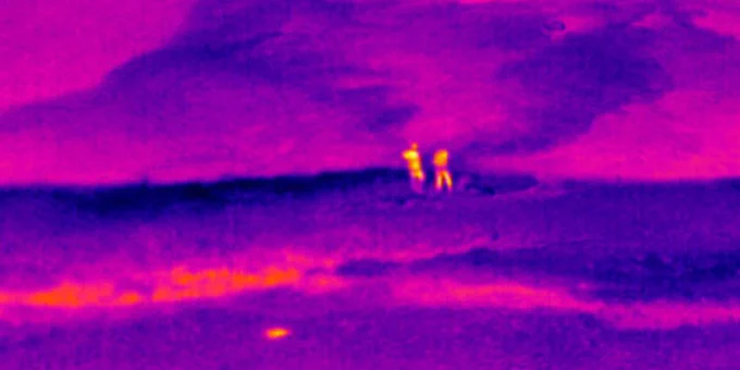 Thermal infrared image of two USGS researchers standing on the coast and looking up over a coastal groundwater plume that is non-visible to the naked eye but is shown in this thermal image from temperature differences between the cooler (blue) groundwater and warmer (pink) ocean water over the coral reefs.