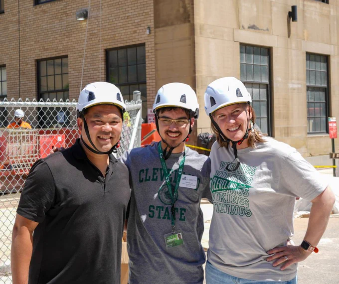 A CSU student and his parents smiling together outside of Fenn tower during orientation. 