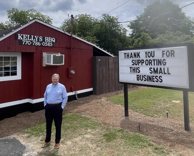 SBA's Jeff Patterson stands in front of Kellys BBQ restaurant with a sign that reads Thank you for Supporting this Small Business. 