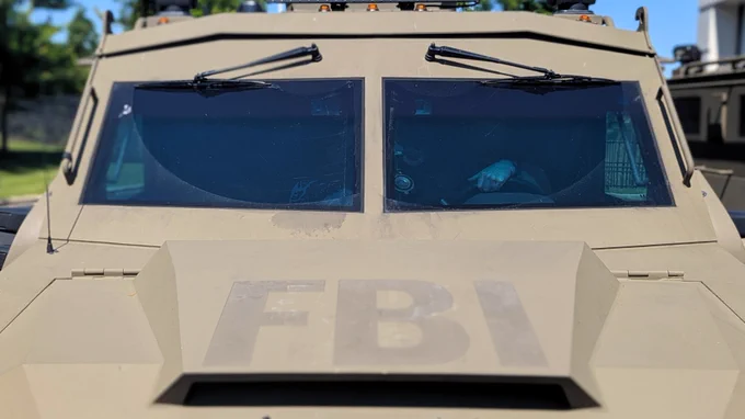 Front view of an armored FBI vehicle with tinted windows under bright daylight.