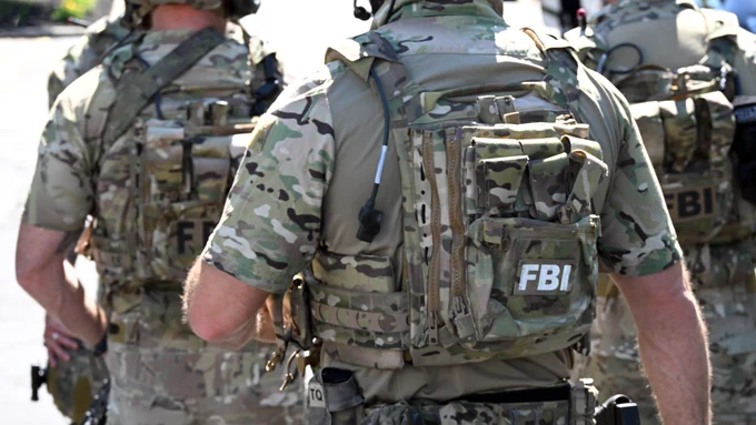 Back view of FBI agents wearing tactical camouflage gear and bulletproof vests during an operation outdoors.