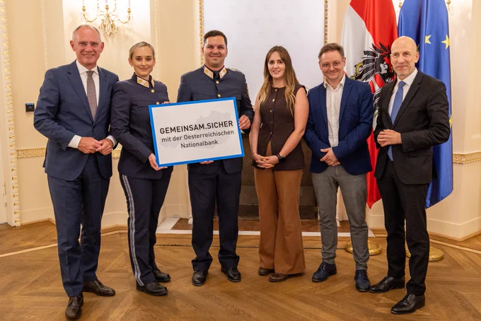 Eine Gruppe von sechs Personen in Geschäftskleidung posiert gemeinsam mit einem Plakat der Österreichischen Nationalbank.