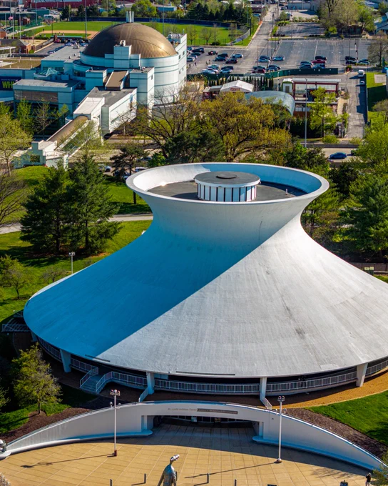 The copper-dome Saint Louis Science Center roof peeks above the centered McDonnell Planetarium as trees dot the landscape behind the iconically curved white roof.